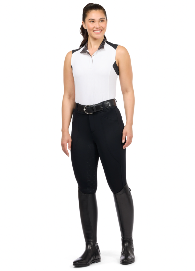Woman wearing a white sleeveless top and black riding pants with tall boots on a white background