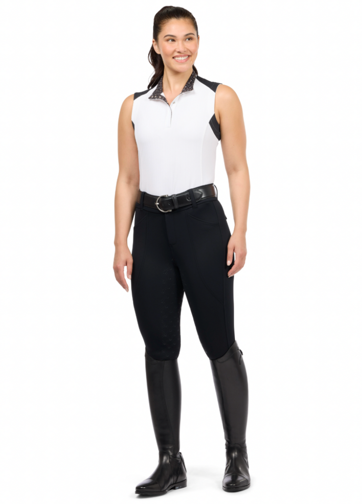 Woman wearing a white sleeveless top and black riding pants with tall boots on a white background