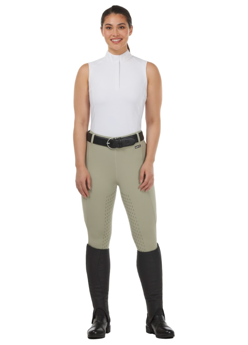 Woman wearing a white sleeveless top and beige riding pants with black boots on a white background