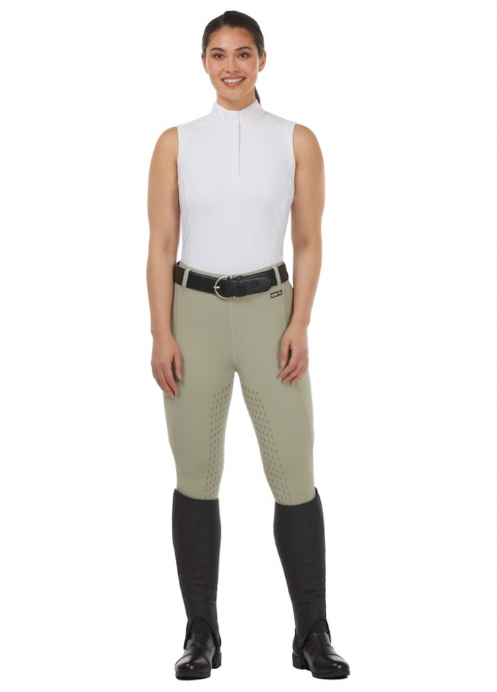 Woman wearing a white sleeveless top and beige riding pants with black boots on a white background